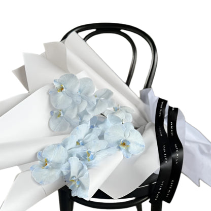 Bouquet of light blue flowers on a black chair with white paper, against a concrete wall.