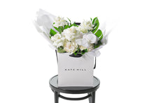 Our white and green ALEXANDRA gift flower bouquet sitting on a black bentwood chair. Large white and green gift bouquet packed full of the freshest and finest flowers in white and green tones including roses, hydrangeas, white phalaenopsis orchid and lush green foliage. Beautifully gift wrapped in our bespoke Kate Hill style and placed into our flower bag.