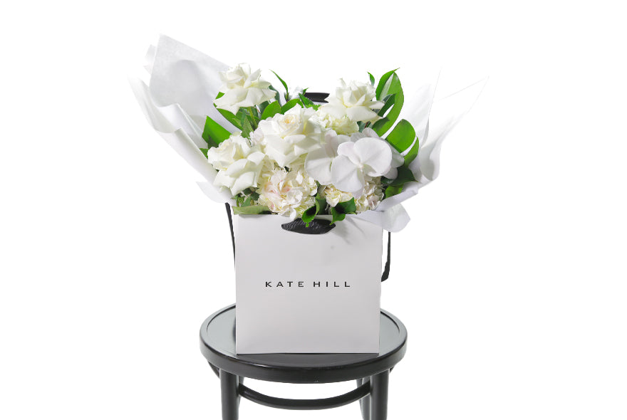 Our white and green ALEXANDRA gift flower bouquet sitting on a black bentwood chair. Large white and green gift bouquet packed full of the freshest and finest flowers in white and green tones including roses, hydrangeas, white phalaenopsis orchid and lush green foliage. Beautifully gift wrapped in our bespoke Kate Hill style and placed into our flower bag.