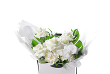 Close up image of the ALEXANDRA flower bouquet. Showing exactly whats designed in the bouquet and the quality of design and flower. Our white and green ALEXANDRA gift flower bouquet sitting on a black bentwood chair. Large white and green gift bouquet packed full of the freshest and finest flowers in white and green tones including roses, hydrangeas, white phalaenopsis orchid and lush green foliage. Beautifully gift wrapped in our bespoke Kate Hill style and placed into our flower bag.