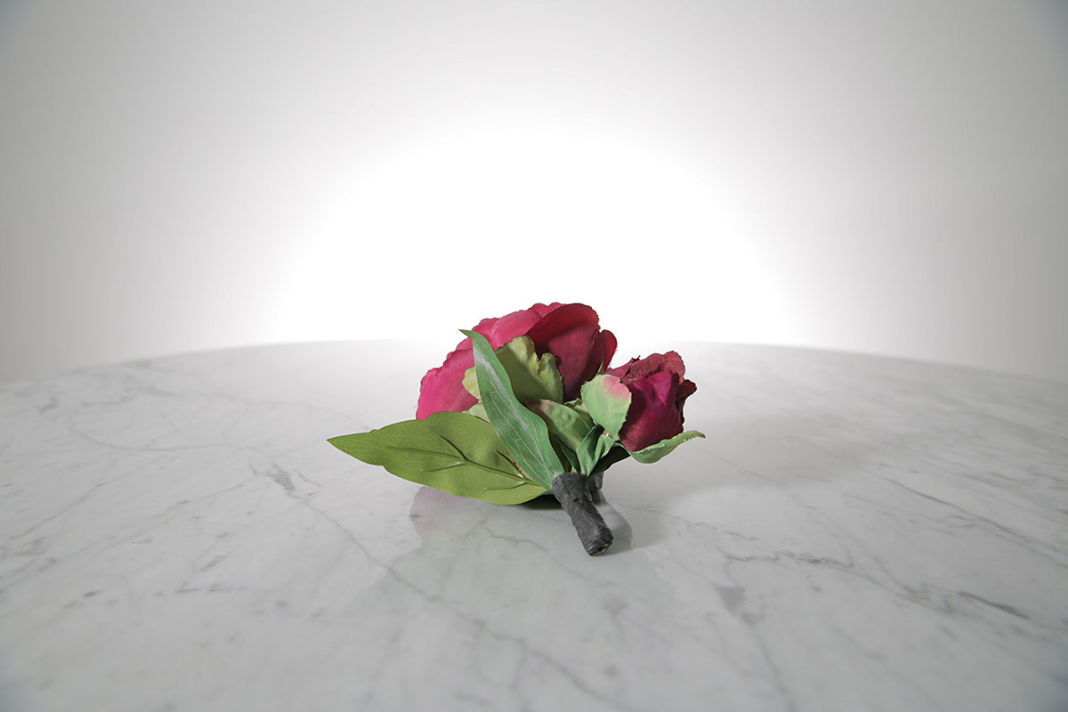Kate Hill Flowers – artificial burgundy peony rose buttonhole flower with green leaf backing and pearl pin on marble table setting. 