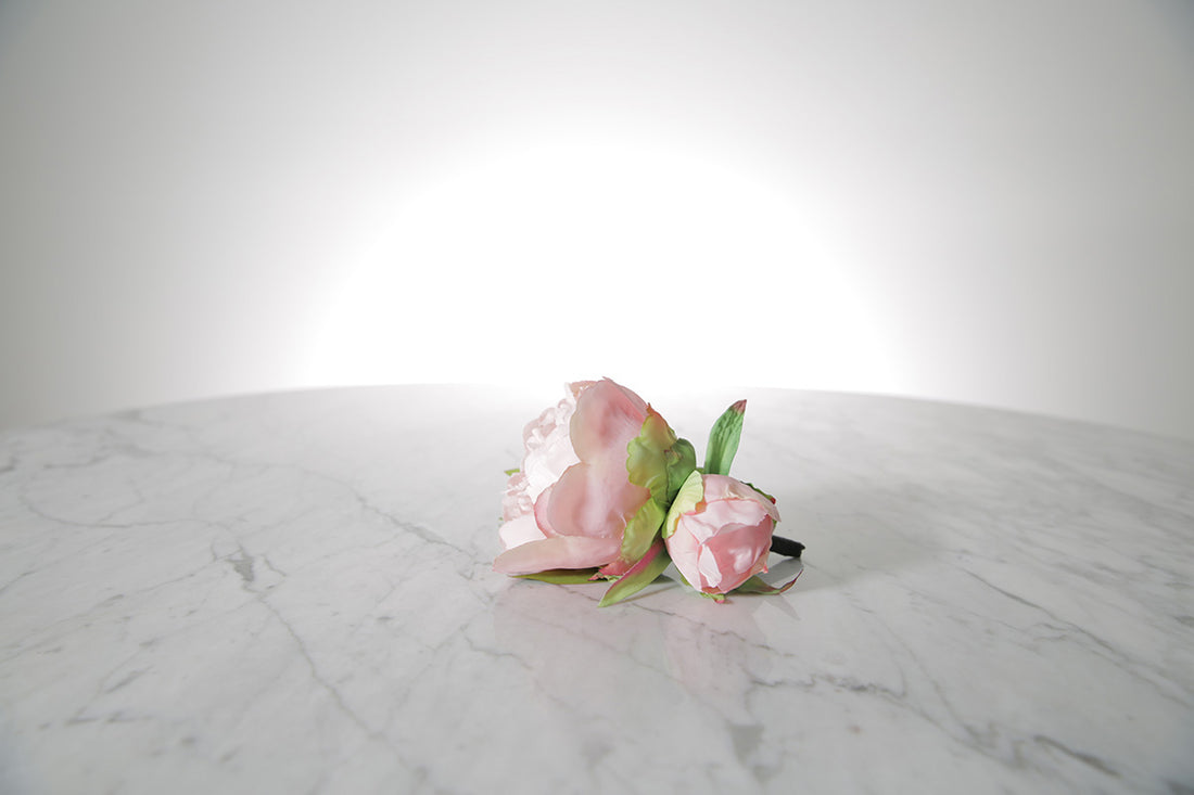 Kate Hill Flowers – artificial pale pink peony rose buttonhole flowers with green leaf backing and pearl pin set on a marble table.