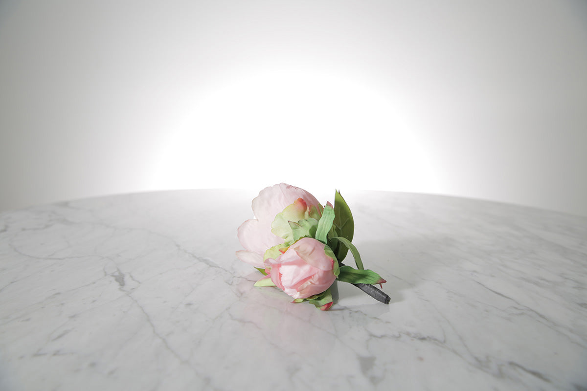 Kate Hill Flowers – artificial pale pink peony rose buttonhole flowers with green leaf backing and pearl pin set on a marble table.