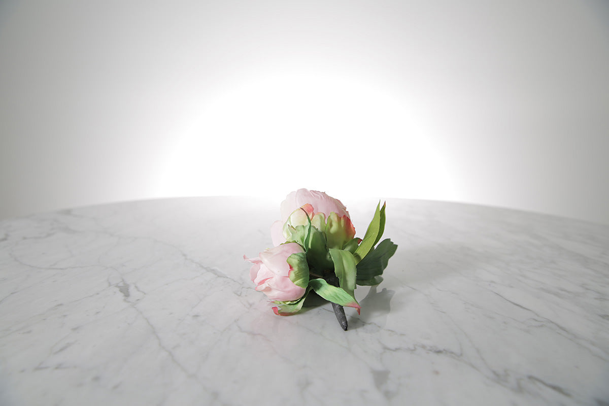 Kate Hill Flowers – artificial pale pink peony rose buttonhole flowers with green leaf backing and pearl pin set on a marble table.