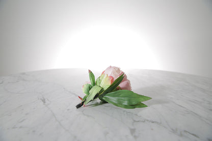 Kate Hill Flowers – artificial pale pink peony rose buttonhole flowers with green leaf backing and pearl pin set on a marble table.