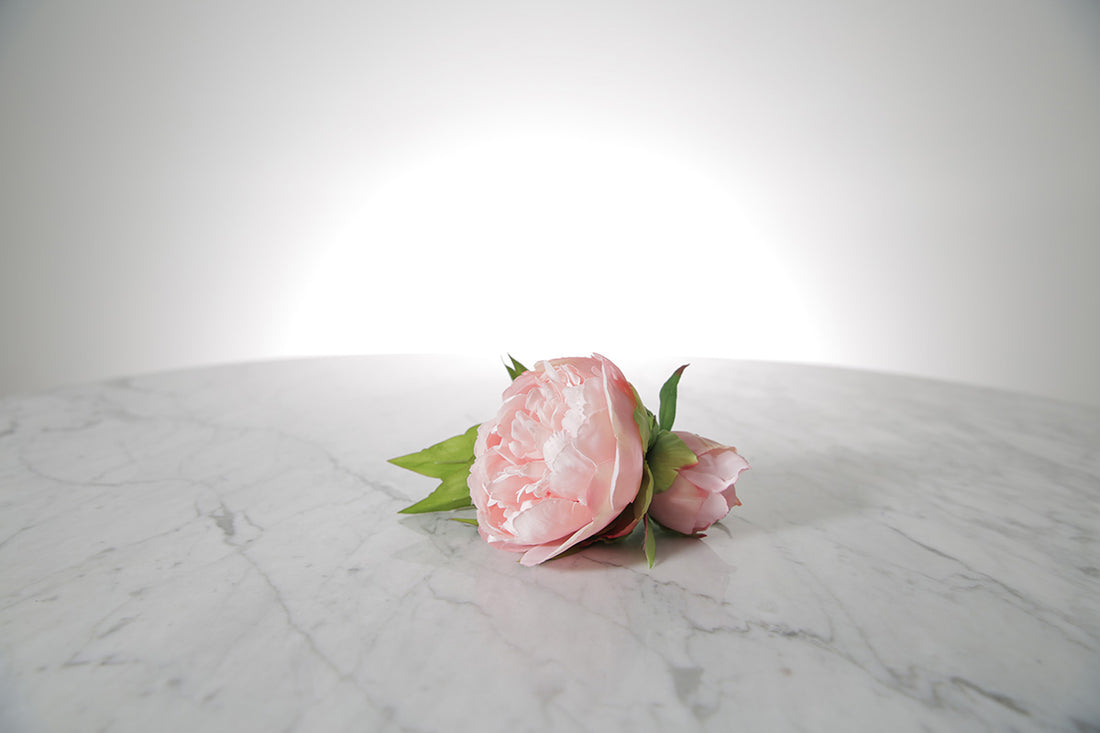 Kate Hill Flowers – artificial pale pink peony rose buttonhole flowers with green leaf backing and pearl pin set on a marble table.