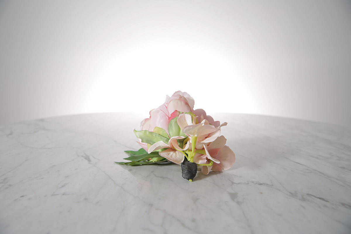 Kate Hill Flowers – pink spray rose buttonhole flowers with black-taped stem and pearl pin on marble table setting.