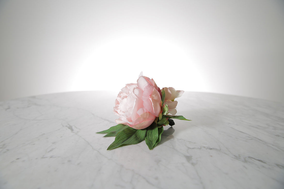 Kate Hill Flowers – pink spray rose buttonhole flowers with black-taped stem and pearl pin on marble table setting.