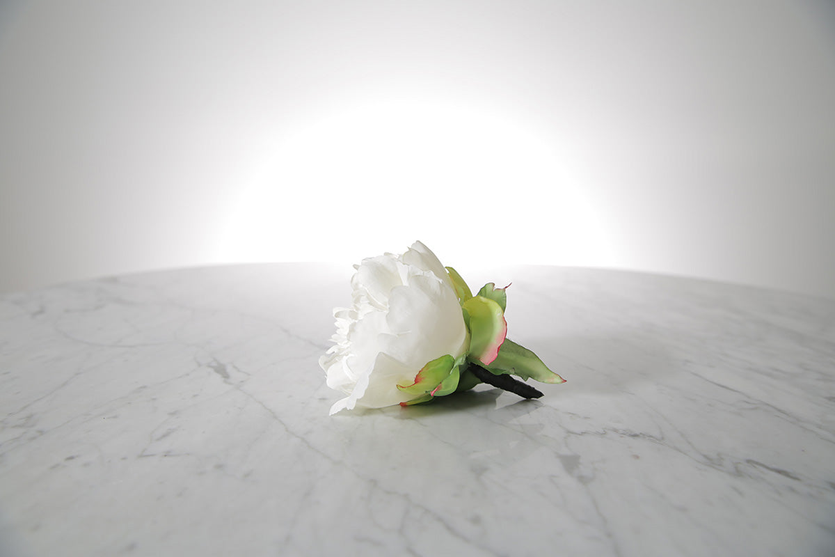 Kate Hill Flowers – artificial white peony rose buttonhole flower with green leaf backing and pearl pin set on a marble table top.