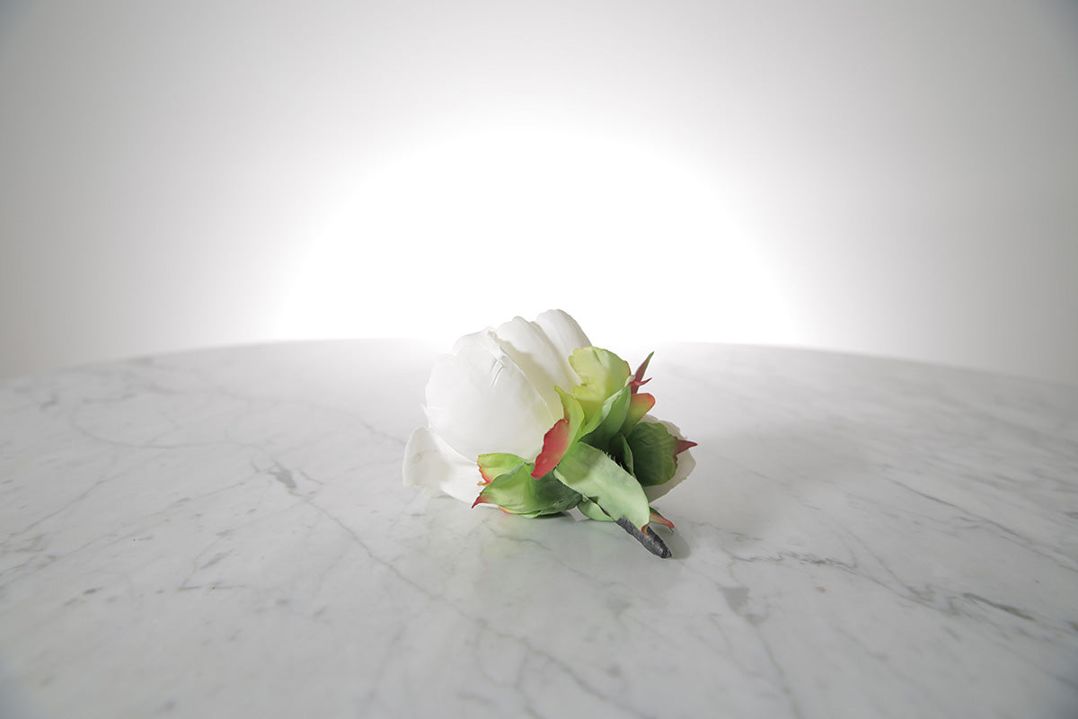 Kate Hill Flowers – artificial white peony rose buttonhole flower with green leaf backing and pearl pin set on a marble table top.