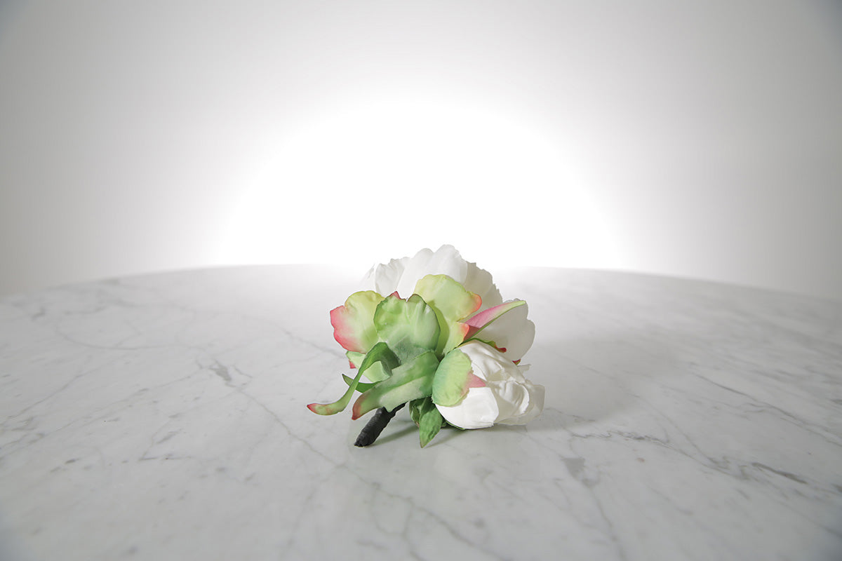 Kate Hill Flowers – artificial white peony rose buttonhole flower with green leaf backing and pearl pin set on a marble table top.