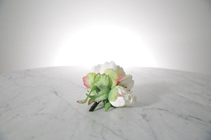 Kate Hill Flowers – artificial white peony rose buttonhole flower with green leaf backing and pearl pin set on a marble table top.