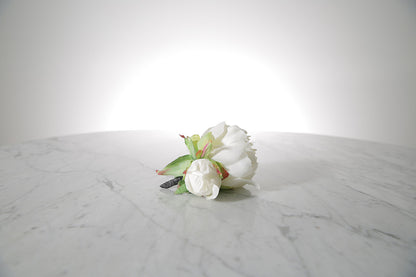 Kate Hill Flowers – artificial white peony rose buttonhole flower with green leaf backing and pearl pin set on a marble table top.