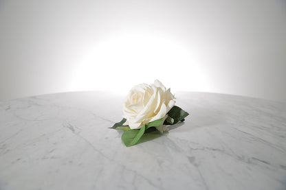 Kate Hill Flowers – artificial white rose buttonhole flower with green leaf backing, black-taped stem and pearl pin on a marble table setting.