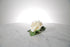 Kate Hill Flowers – artificial white rose buttonhole flower with green leaf backing, black-taped stem and pearl pin on a marble table setting.