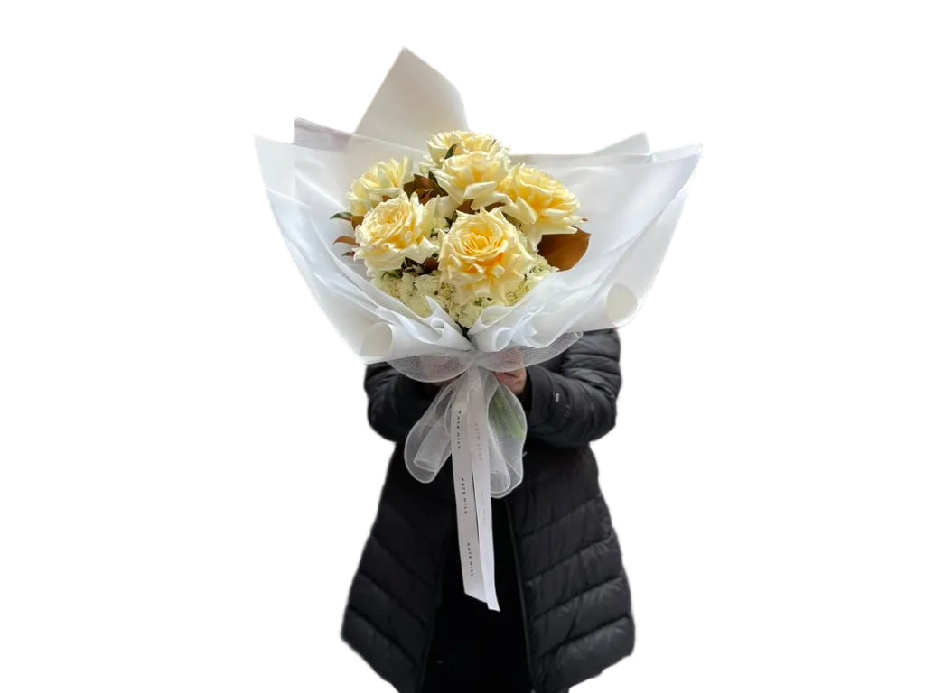 Florist holding our August signature flower bouquet featuring lemon and cream tones, wrapped in white signature wrapping.