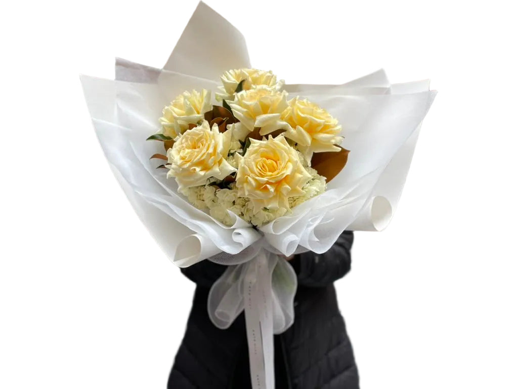 Close up of florist holding our August signature flower bouquet featuring lemon and cream tones, wrapped in white signature wrapping.