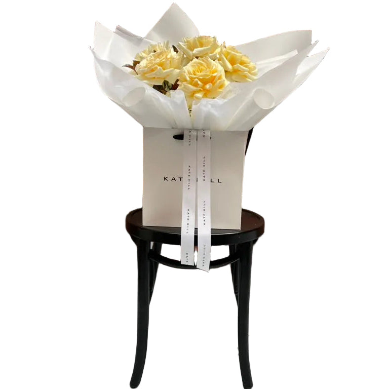 August Birthday Bouquet featuring lemon and cream tones sitting on a black bentwood chair.