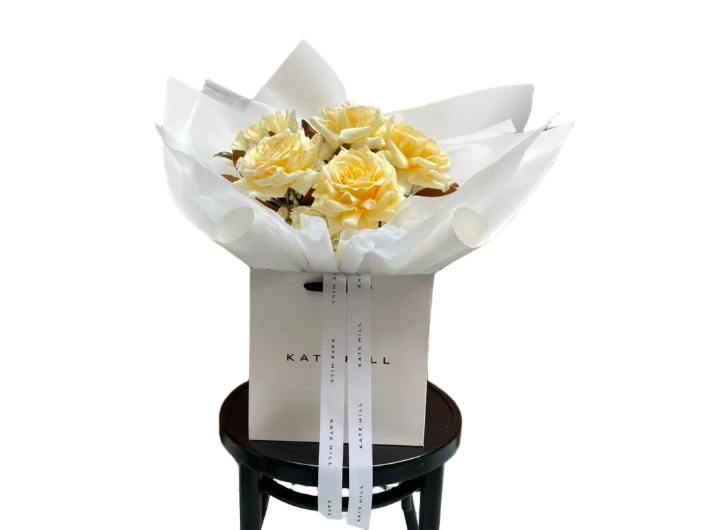 Close up image of our August Birthday Bouquet in lemon and cream tones, sitting on a black bentwood chair.