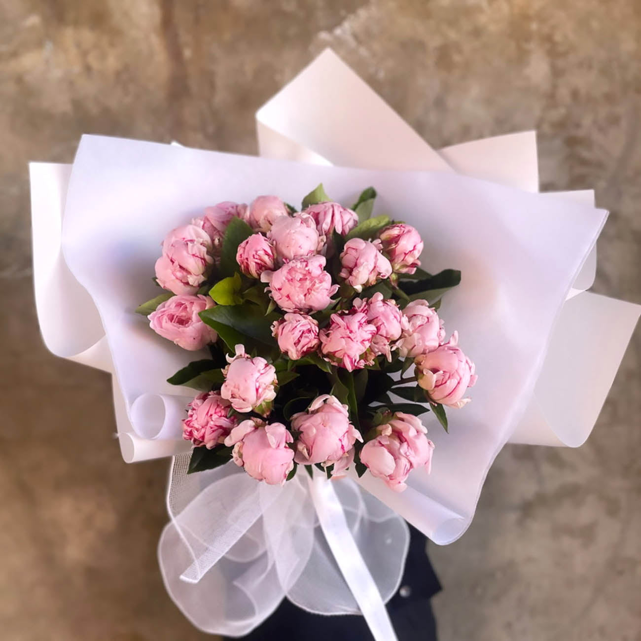Bouquet of pink flowers wrapped in white paper on a textured surface