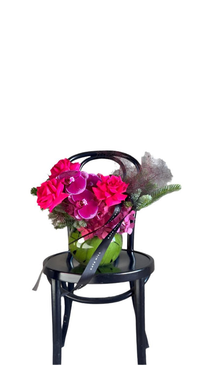 A jewel toned ball vase design sitting on a black bentwood chair with a white wall background.