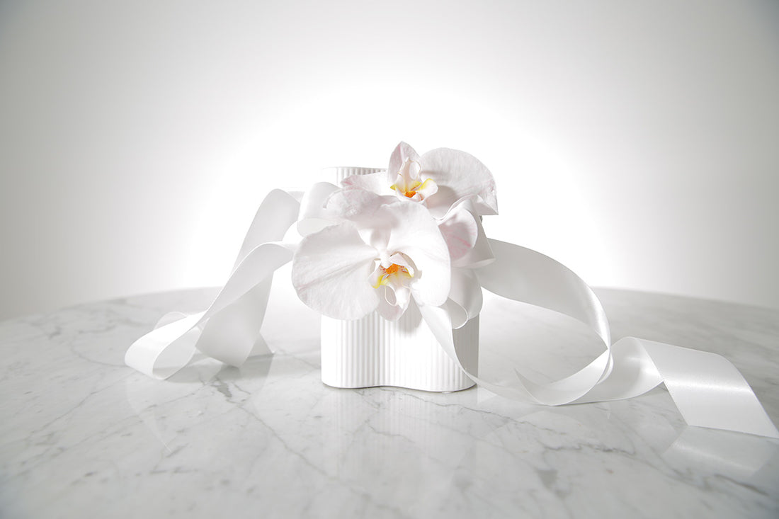 Kate Hill Flowers blush Phalaenopsis orchid wrist corsage with satin bows on a silver elastic wristlet on a marble surface