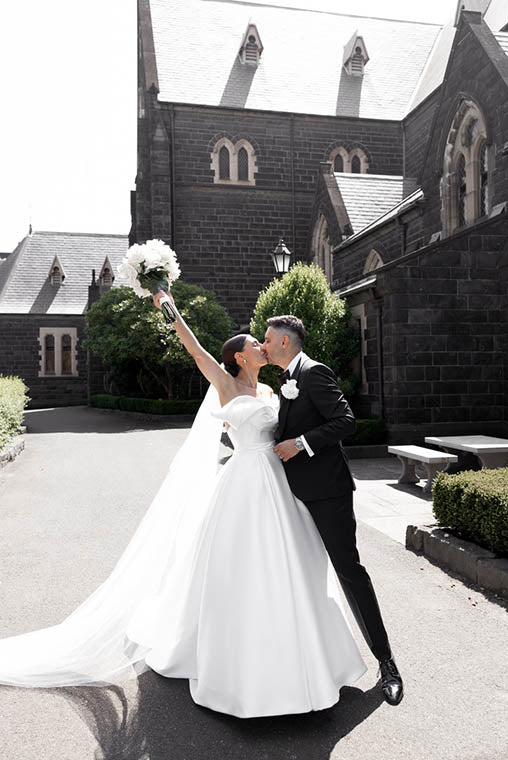 Melbourne bride holding a white rose bridal bouquet kissing husband at wedding ceremony