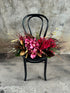 A black bentwood chair with the GARNET rich red tablescape sitting on chair, against a concrete wall. 