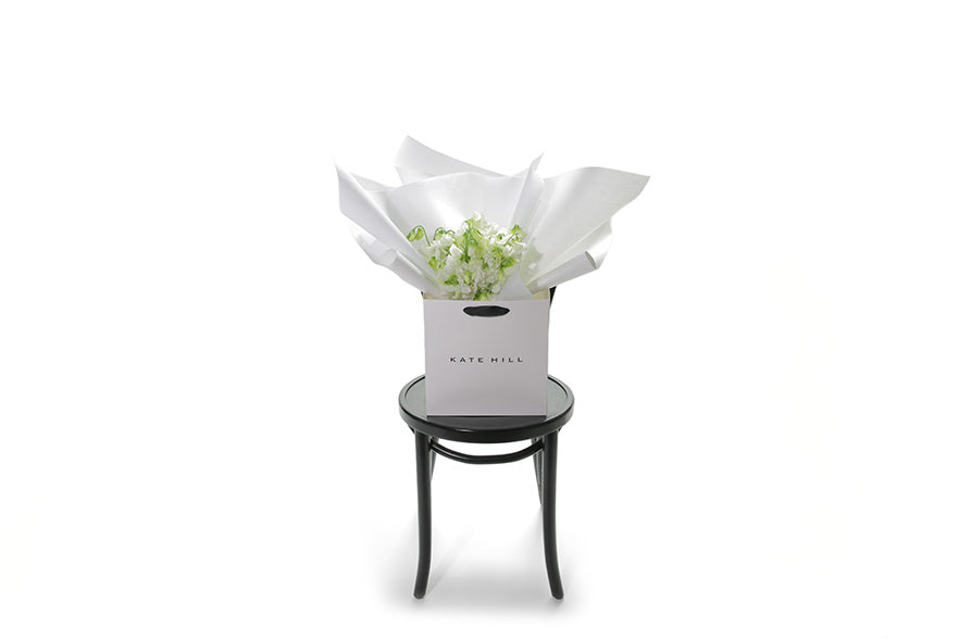Wide images of the Camila sweetpea flower bouquet. Fragrant bouquet of white sweetpea sitting on a black bentwood chair. Bouquet is beautifully wrapped in the Kate Hill signature wrapping and placed into a Kate Hill flower bag. Our CAMILA Sweetpea Flower Bouquet is an all rounded, simple dome posy featuring fragrant White Sweet-pea. A petite, sweet, fragrant posy perfect for those who love elegant fragrance and who appreciate Sweet-peas for their soft beauty and scent.