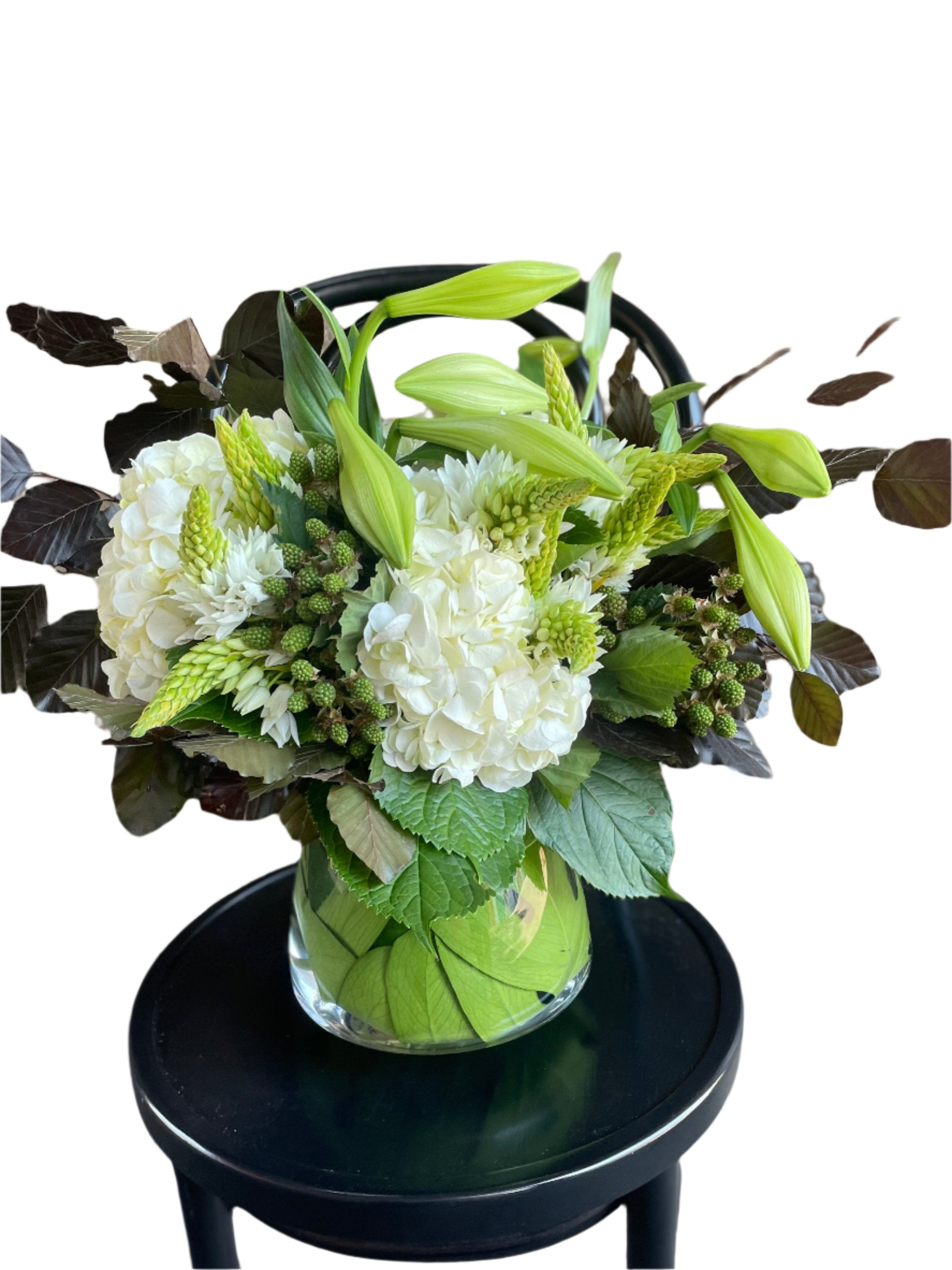 Close up image of our christmas flower vase design displaying white and green festive flowers sitting on a black bentwood chair with a white background.