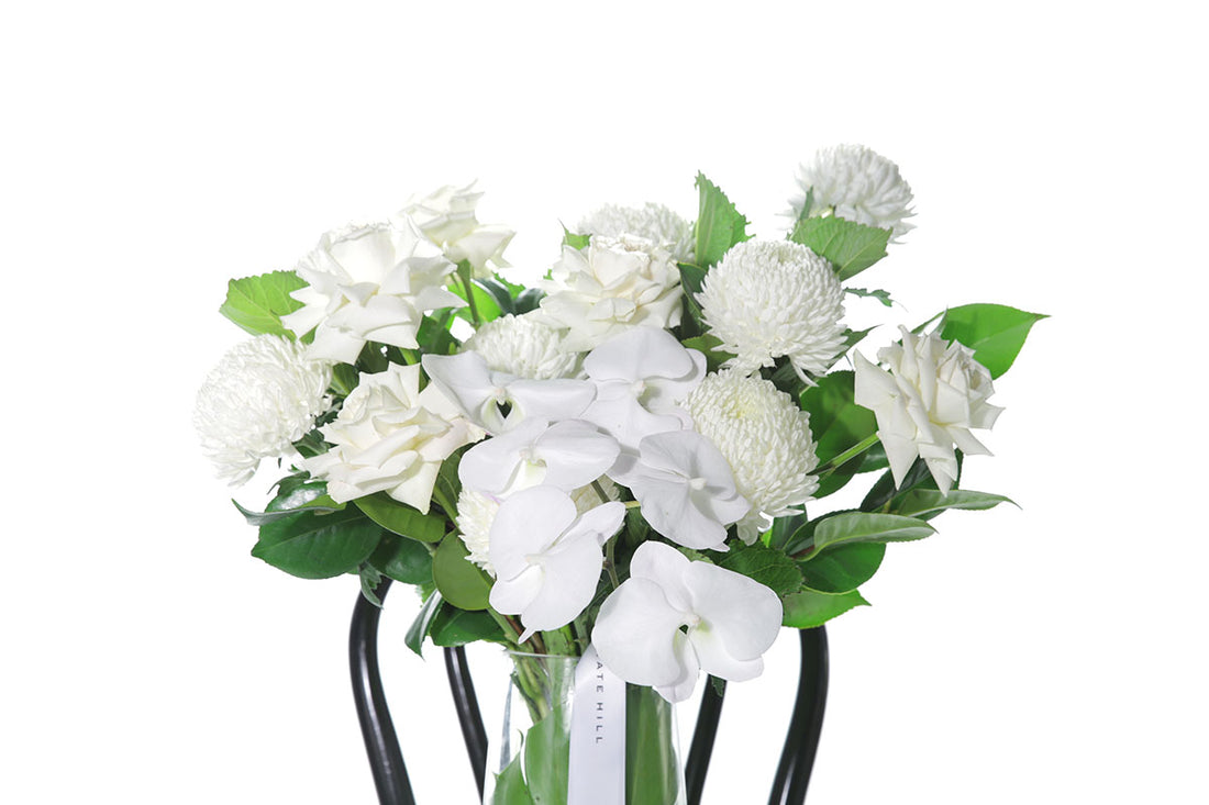 Kate Hill Flowers – large white and green birthday vase with roses, chrysanthemums and orchids in a monstera-lined tapered glass.