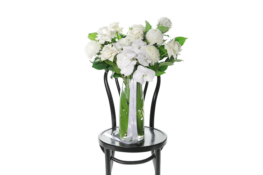 Kate Hill Flowers – large white and green birthday vase with roses, chrysanthemums and orchids in a monstera-lined tapered glass.