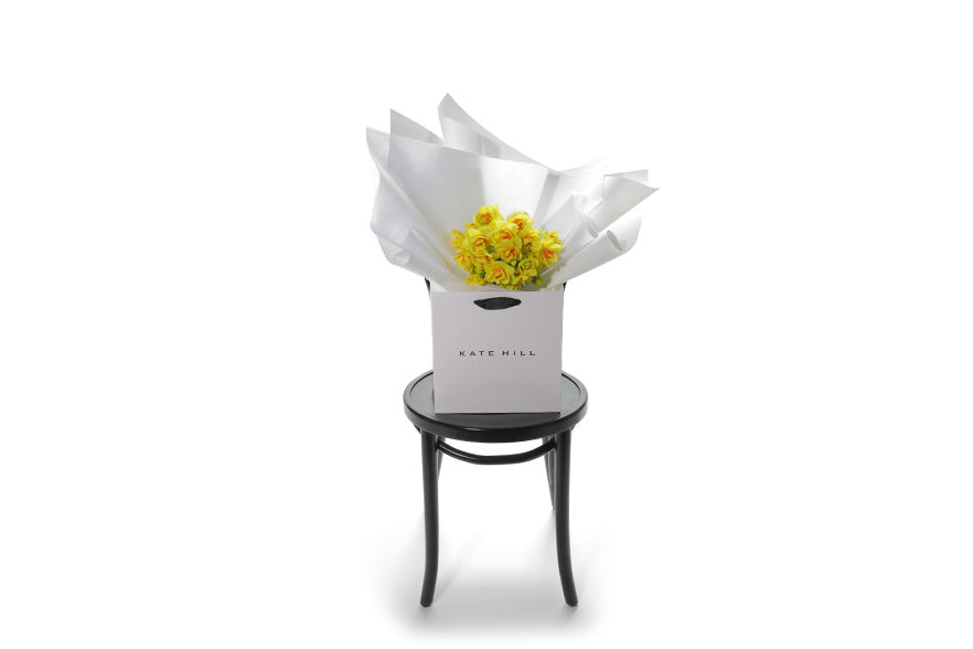 Wide image of the DAFFODIL flower bunch sitting on a black bentwood chaor. Petite posy of wrapped Daffodils, sitting on a black bentwood chair. Classed as a small in size, the DAFFODIL is a hand tied collection of 3 bunches of DAFFODILS which are beautifully gift wrapped in our signature wrapping. Yellow double daffodils in image.