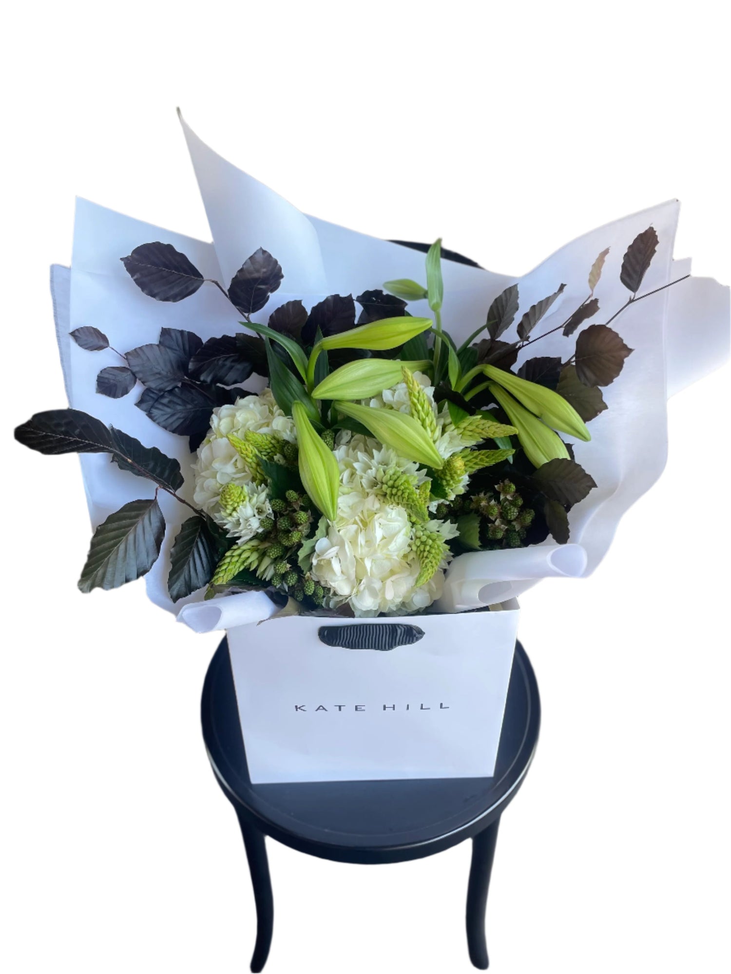 A festive white and green bouquet, beautifully wrapped in signature white wrapping sitting on a black bentwood chair with a white wall background.