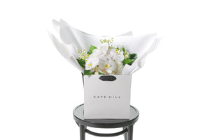 White and green with a pop of yellow lemon medium sized bouquet, beautifully wrapped in white signature presentation. Bouquet is placed into Kate Hill flower bag to ensure the bouquet remains fresh in water. Bouquet bag is sitting on a black bentwood chair with a white background.
