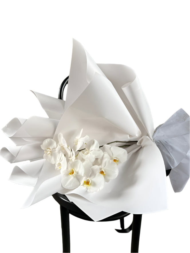 Bouquet of white flowers wrapped in white paper on a black stool against a textured wall.