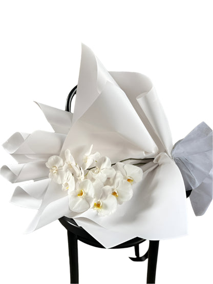 Bouquet of white flowers wrapped in white paper on a black stool against a textured wall.