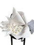 Bouquet of white flowers wrapped in white paper on a black stool against a textured wall.