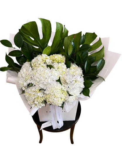 An angle from above of the white hydrangea birthday bouquet, sitting on a black bentwood with white background.