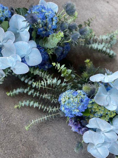 Florist holding a table hedge of blue seasonal flowers and grey blue foliages. Flowers laying on concrete floor.