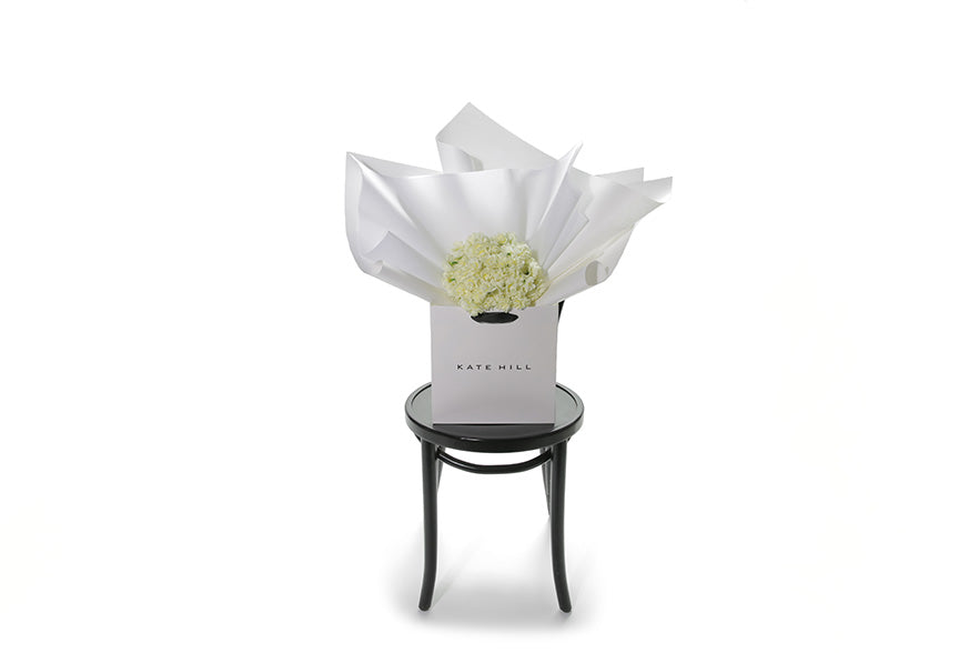 Wide image of the CLAIRE flower bunch sitting on a black bentwood chair. Petite posy of fragrant Erlicheer beautifully wrapped in signature white wrapping. The CLAIRE Flower Bouquet is a short, petite posy bunch featuring gift wrapped Erlicheer which make a beautiful gesture gift for any occasion. Or a beautiful cut bunch for Home.  Classed as a small in size, the CLAIRE is a hand tied collection of 3 bunches of Erlicheer which are beautifully gift wrapped in our signature wrapping. 
