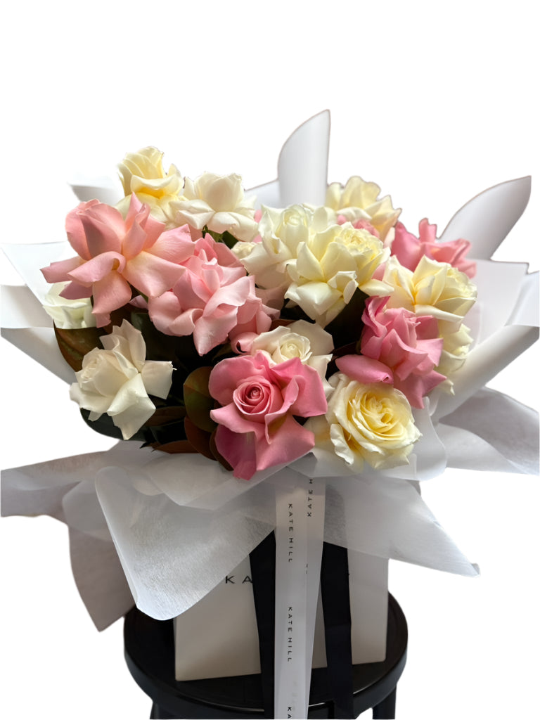 Bouquet of pastel mix pink, buttery lemon and white ross on a black stool against a white wall.