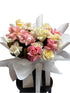 Bouquet of pastel mix pink, buttery lemon and white ross on a black stool against a white wall.