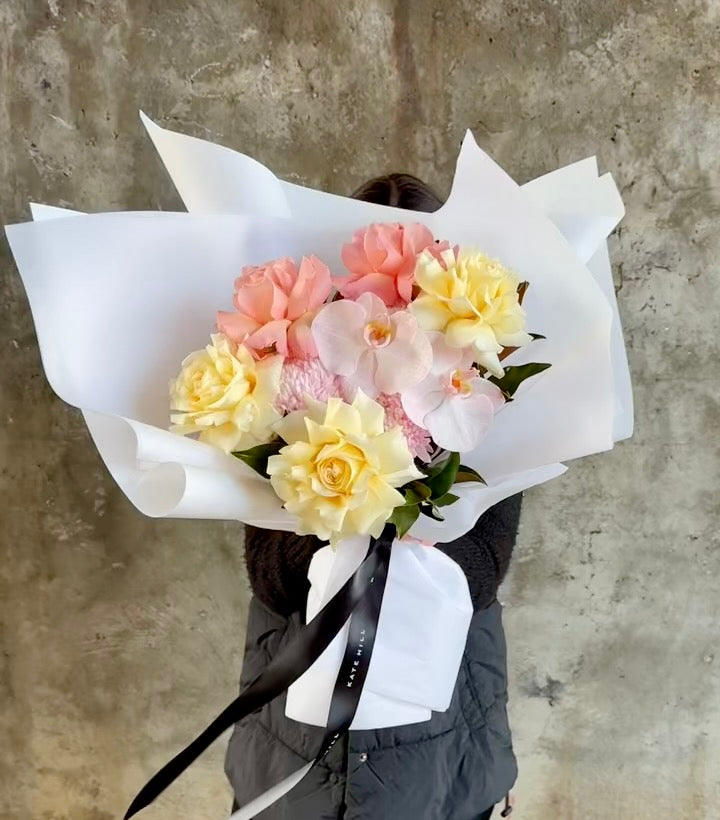 Video of florist holding a blush and lemon pastel gift bouquet in front of a concrete wall.