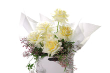 Close up image of GIGI butter bouquet. Bouquet of lemon butter roses and seasonal foliage, beautifully wrapped in white signature wrapping. Bouquet displayed in kate hill flower bag, sitting on black bentwood chair with white background.