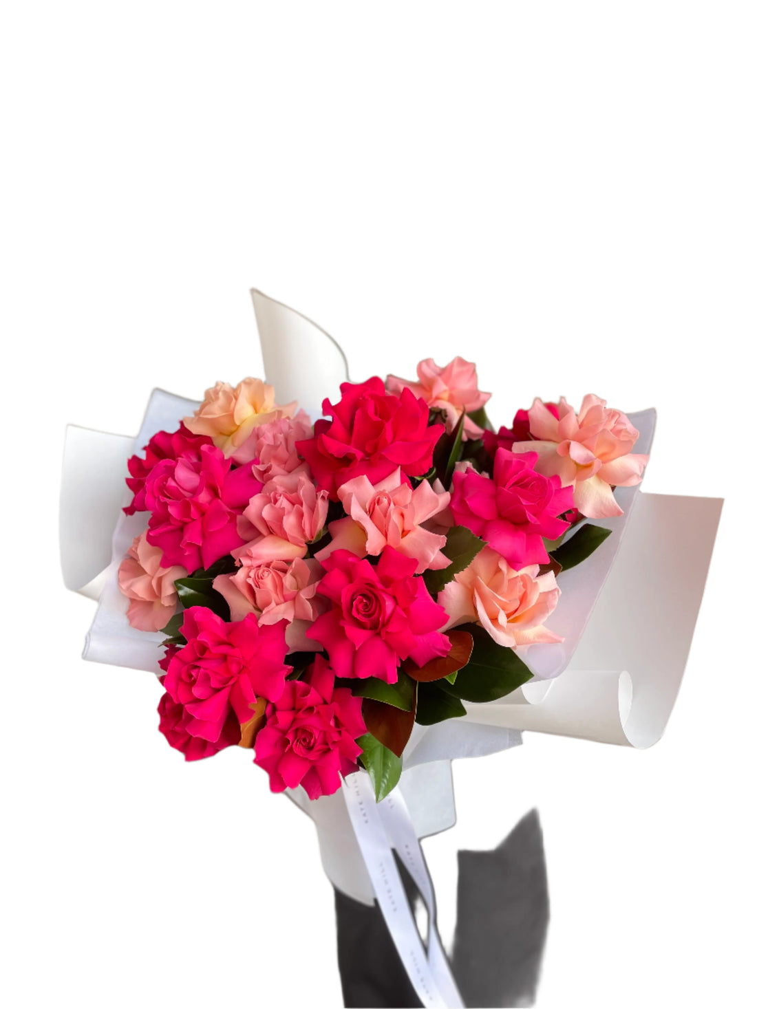 20 stems of hot pink and watermelon roses beautifully presented as a large bouquet in white signature wrapping. Florist holding the bouquet against a white wall.