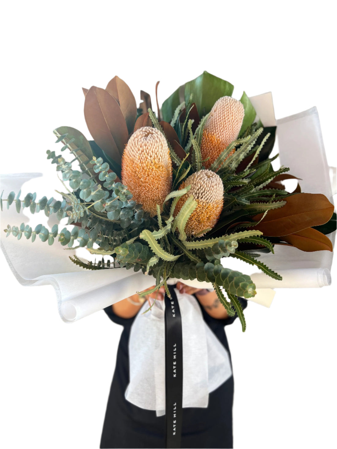 Close up image of a florist wearing black holding a large graduation bouquet displaying Australian native flowers and foliage. Florist standing in front of white wall.