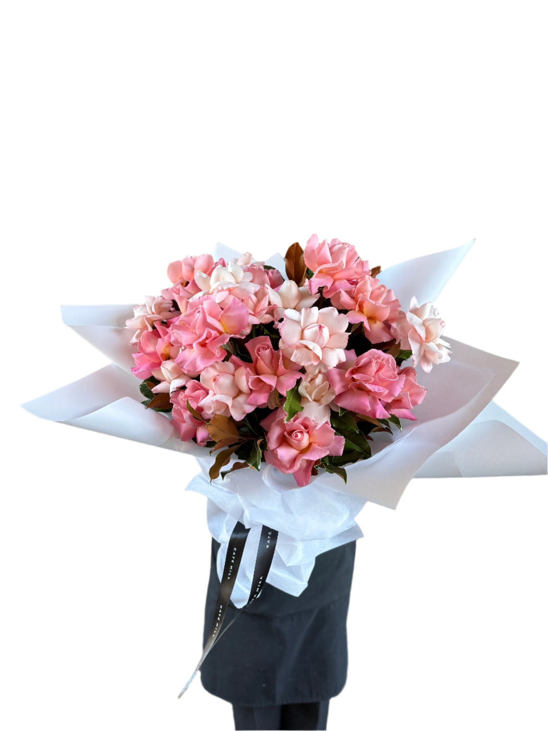 Florist wearing black holding a large graduation bouquet of pale pink, blush and watermelon reflexed roses. Bouquet wrapped in white and bouquet in front of white wall.