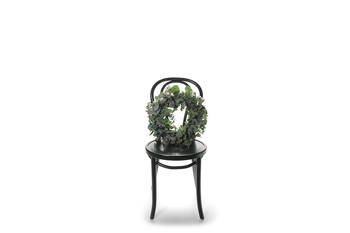 A 45cm Eucalyptus wreath sitting on a black bentwood chair with a white wall background.