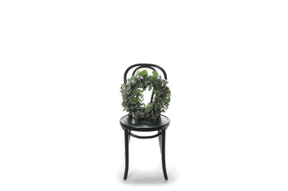 A 45cm Eucalyptus wreath sitting on a black bentwood chair with a white wall background.